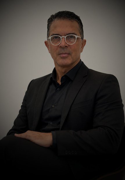 Professor Sammy Oliver em retrato de estúdio, sentado, de blazer preto
